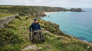 A person using a specialized all-terrain off road wheelchair on a grassy clifftop path along the British coastline.