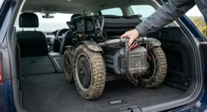 A compact all-terrain electric wheelchair being loaded into the spacious boot of a navy blue UK estate car.