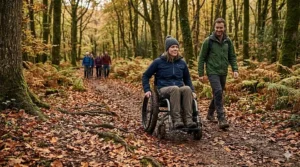 An off road manual wheelchair navigating a muddy woodland track covered in autumn leaves and exposed tree roots.