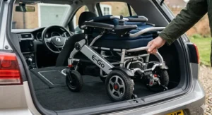 A lightweight electric wheelchair under £1000 being folded and placed into the boot of a silver UK hatchback car.