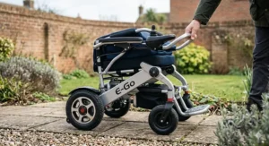 A compact folding electric wheelchair under £1000 being collapsed for easy storage on a paved garden path.