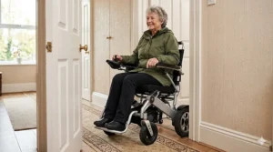 A narrow-frame folding electric wheelchair manoeuvring through a standard wooden doorway inside a UK home.