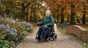 A robust motorised wheelchair for MS users driving across a gravel path in a UK public garden.
