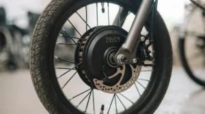 Detailed close-up of a black front wheel hub motor featuring a disc brake and the inscription Velo-X Electric, part of a wheelchair power add-on.