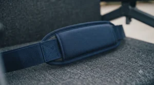 A detailed close-up showing the soft texture and precise stitching of the dark blue padded section of a wheelchair lap strap, resting on the textured grey seat fabric.