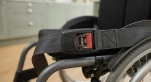 Close-up of the push-button mechanism on a quick-release wheelchair seatbelt for rapid fastening and unfastening.