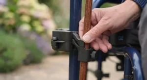 Close-up of a person's hand placing a walking stick into the wheelchair holder.