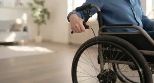 An attendant operating a hub brake system via a lever on the push handle of a transit wheelchair, separate from the standard wheel locks.