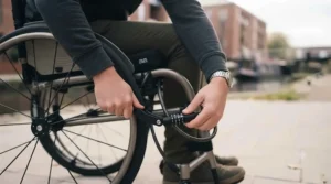 User demonstrating how to properly engage both a wheel lock and a secondary security cable before leaving a wheelchair unattended.