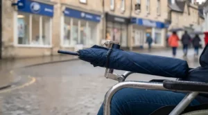 A foldable wheelchair umbrella neatly collapsed and stored alongside the chair when the rain stops.
